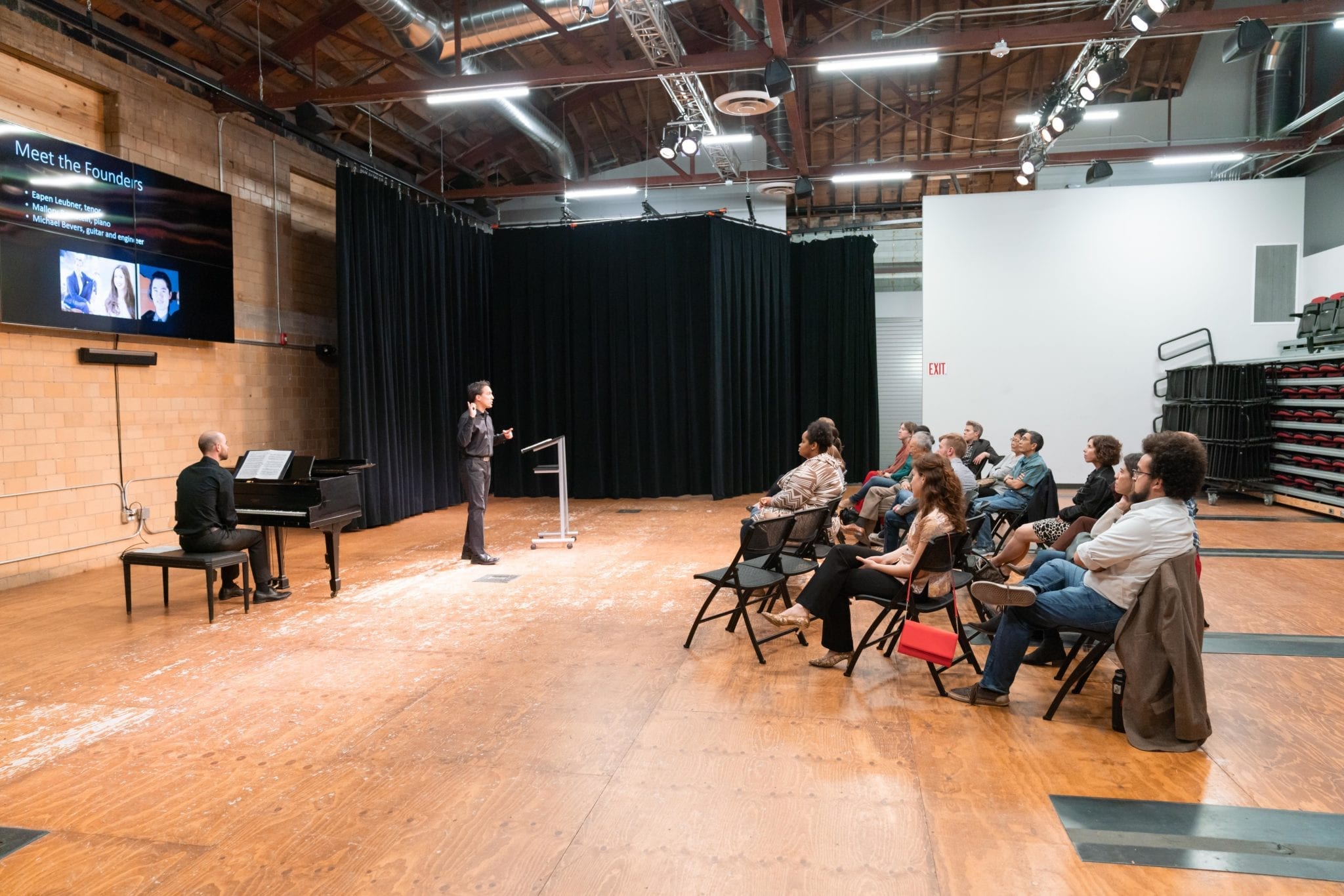 Art Song Colorado's Eapen Leubner performs for an audience seated in a large industrial room with wooden flooring and a grand piano.