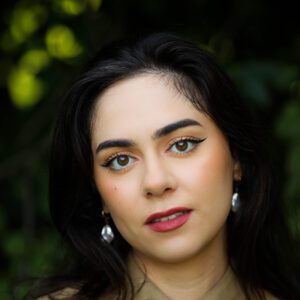 Melanie Dubil, a light-skinned woman with natural-esque makeup and long dark hair poses with a neutral expression.